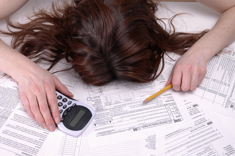 Woman at desk with head down on tax forms, holding a pencil and calculator.