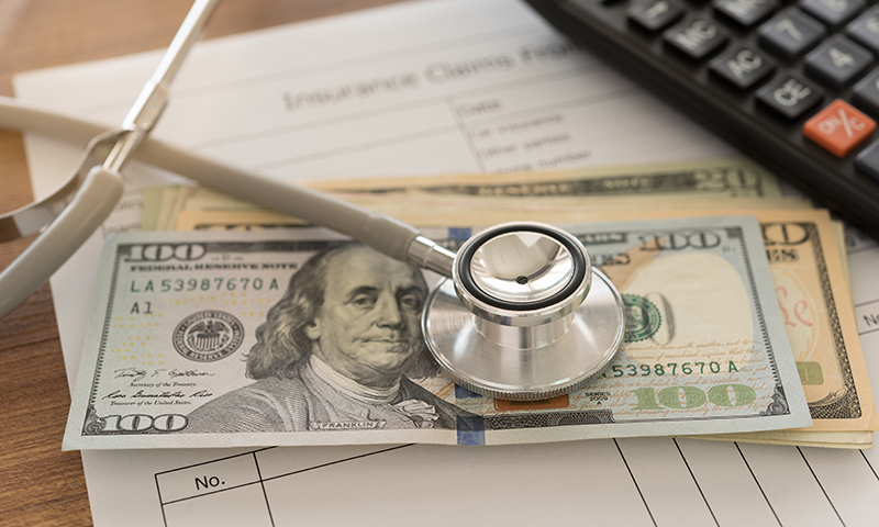 stethoscope on top of stack of cash over an Insurance Claims statement