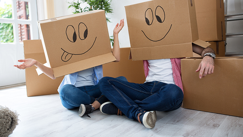 Couple with moving boxes on their heads with happy faces drawn on them