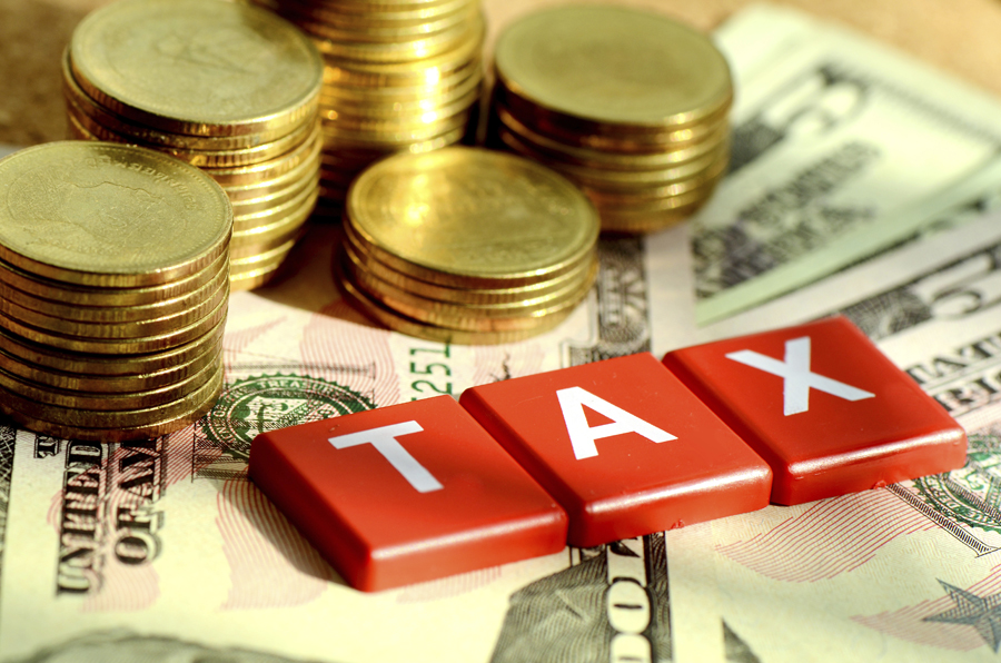 The word TAX spelled out with tiles on paper money and next to a stack of coins