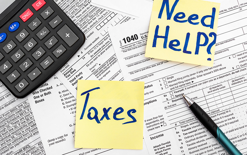 Need Help? and Taxes written on sticky notes on top of tax forms