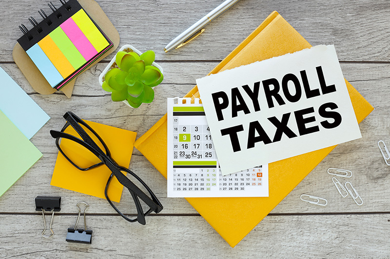 Payroll Taxes written on paper with office supplies in background