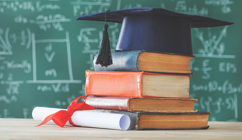 Stack of books, graduation hat, and rolled up diploma