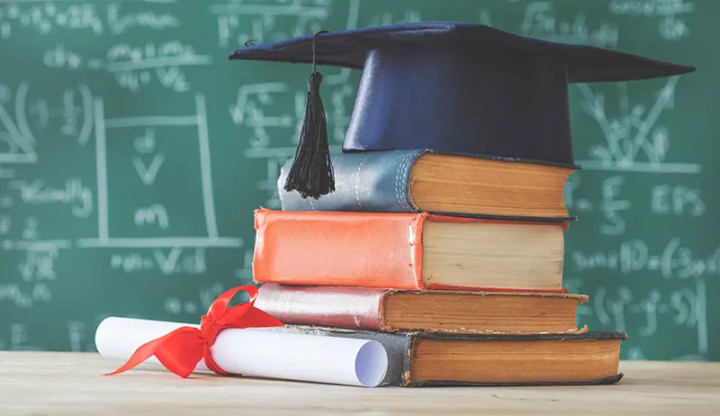 Stack of books, graduation hat, and rolled up diploma