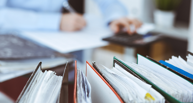 Auditor writing on paper with binders on his desk