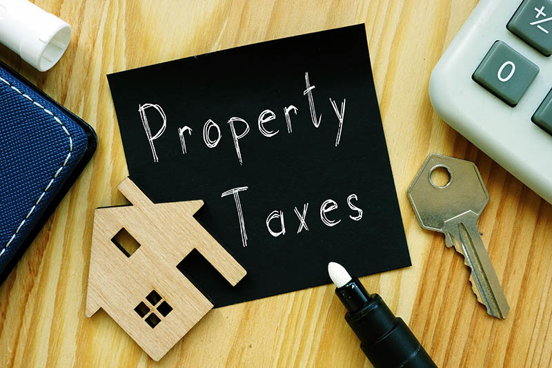 Property Taxes Sign next to wooden house, key, pen, and calculator
