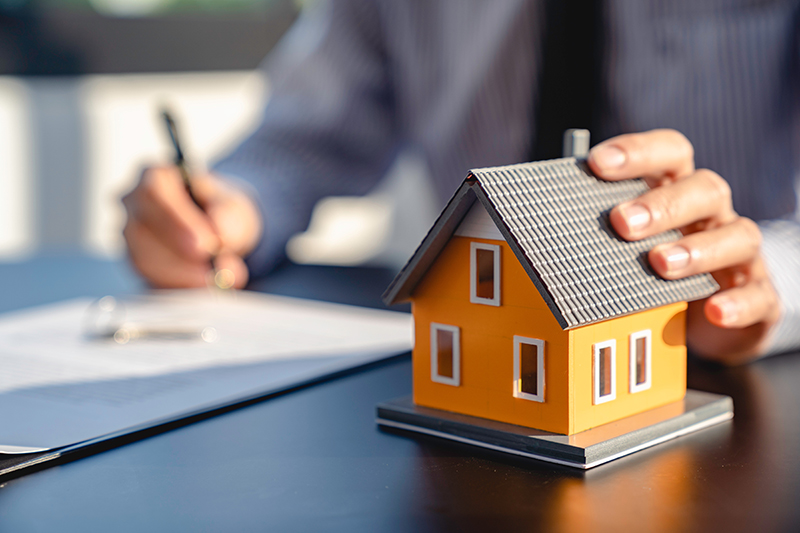 Man filling out paperwork with hand on model house