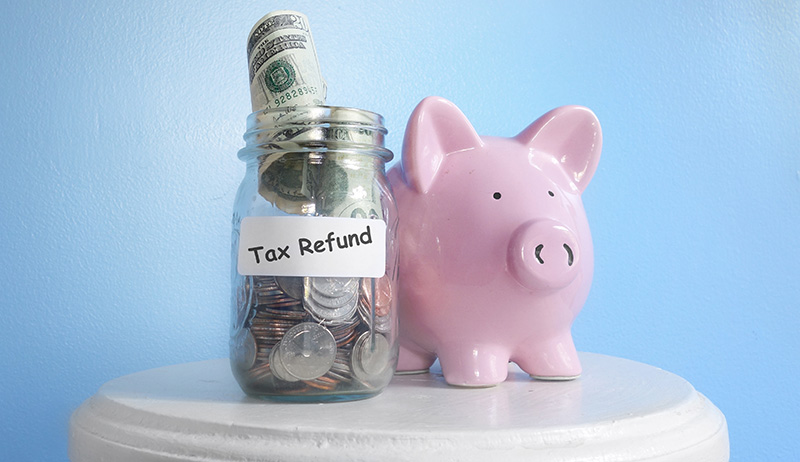 Tax Refund Written on Jar next to a Piggy Bank